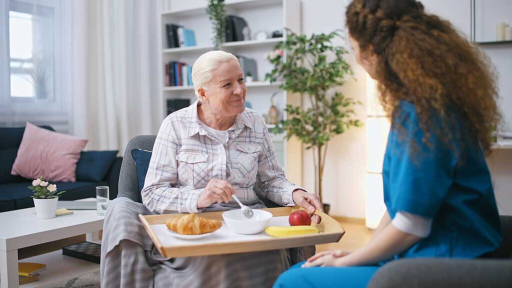 An older adult and a family member having a thoughtful conversation at a dining table with paperwork and medication visible.