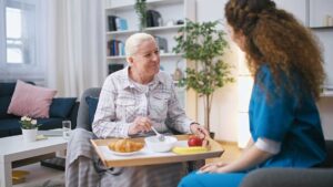 An older adult and a family member having a thoughtful conversation at a dining table with paperwork and medication visible.