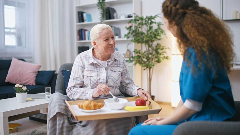 An older adult and a family member having a thoughtful conversation at a dining table with paperwork and medication visible.